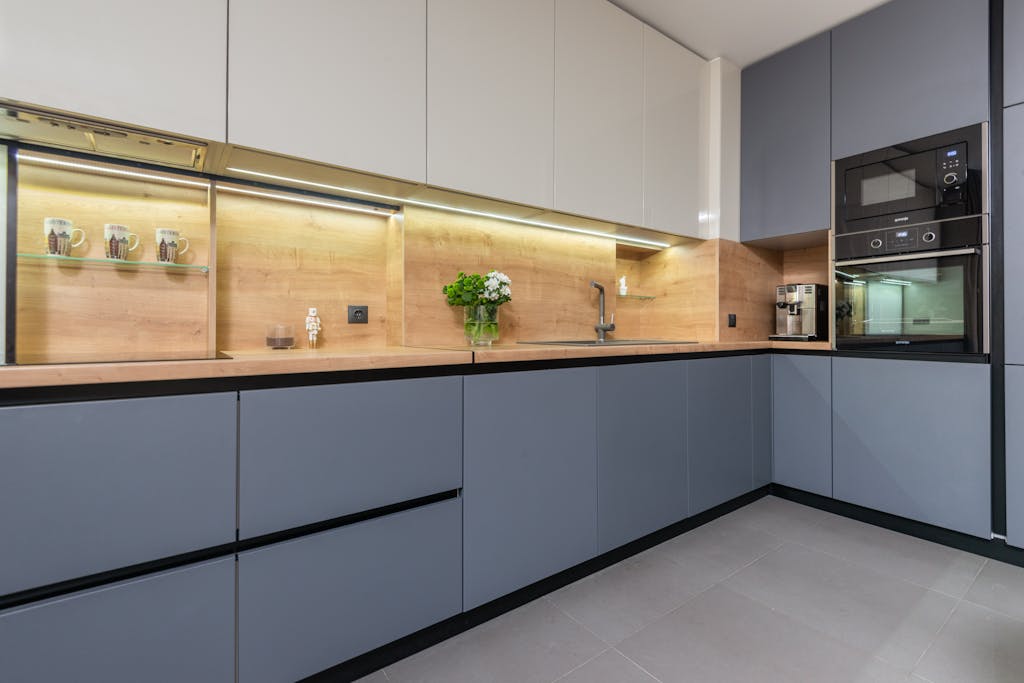 Modern kitchen with cabinets and microwave oven against flowers and decorative mugs on shelf in light house