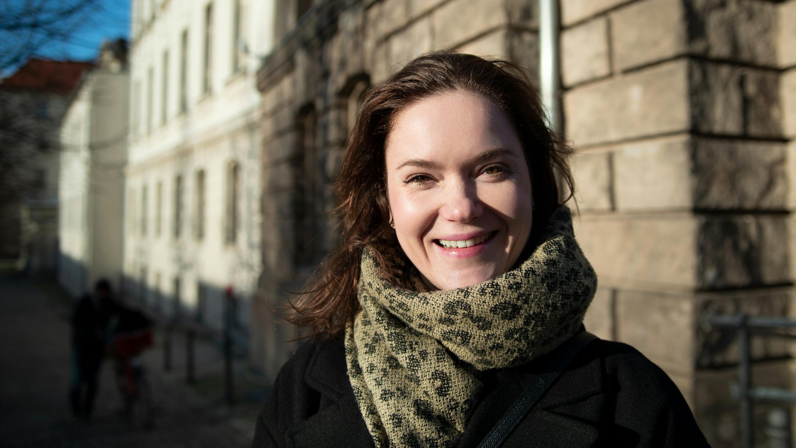 Young woman smiling on a Berlin street during winter, enjoying the bright day.